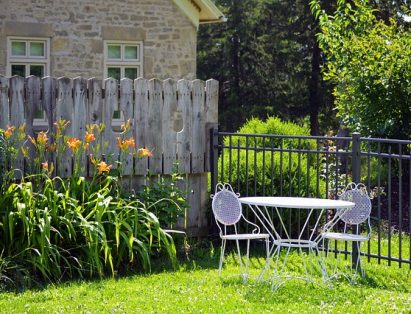 A landscaped backyard with trimmed grass, flowers, and a white furniture set