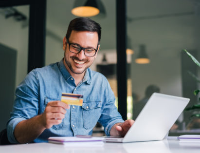 Happy man on laptop and holding a card after paying for a commercial junk removal services